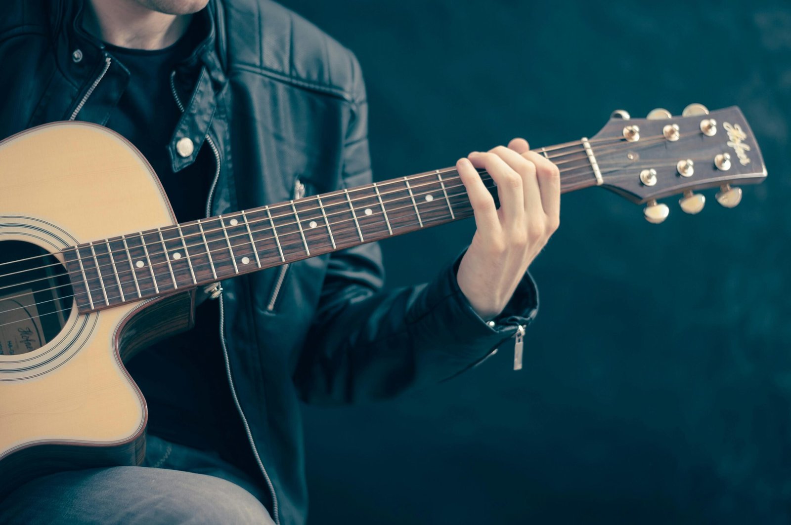 Close-up of a musician playing an acoustic guitar, wearing a leather jacket.